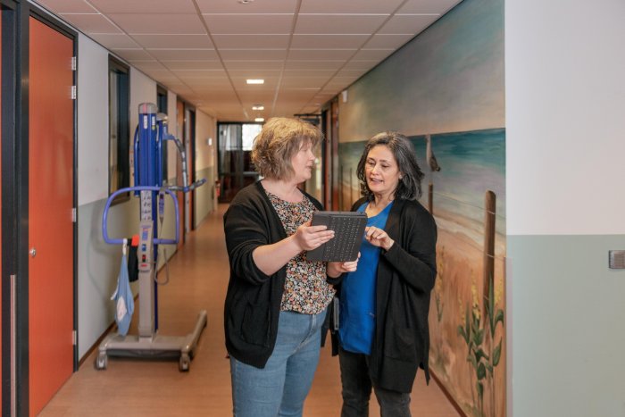 Twee vrouwen staan in een gang te kijken naar een tablet 