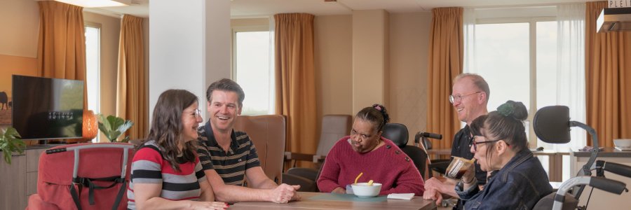 5 mensen zitten allemaal rond de tafel te lachen met elkaar